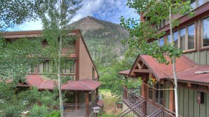 A mountain lodge with multiple wooden buildings, a covered deck, and a staircase leading to a balcony. - The Burly Bear | AC, Pool, Hot Tub, Golf & Ski (Durango)