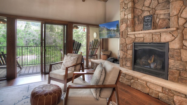 A cozy living room with a stone fireplace, comfortable seating, and a television. - The Burly Bear | AC, Pool, Hot Tub, Golf & Ski (Durango)