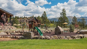 A playground with a slide and swings, surrounded by rocks and trees, with a mountain view in the background. - The Burly Bear | AC, Pool, Hot Tub, Golf & Ski (Durango)