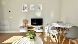 Een moderne woonkamer met een flatscreen televisie, een eettafel met stoelen en een potplant.