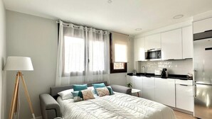 Een moderne slaapkamer met een groot bed, nachtkastjes, een bureau en een kitchenette met een magnetron en een koelkast.