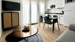 A modern living room with a round dining table, a sofa, and a kitchen area with white cabinets and a microwave. - Vivodomo | Free parking, new, large terrace (Madrid)