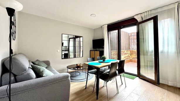 A modern living room with a grey sofa, a dining table with chairs, a TV, and a balcony with a sliding door. - Vivodomo | Free parking, new, large terrace (Madrid)