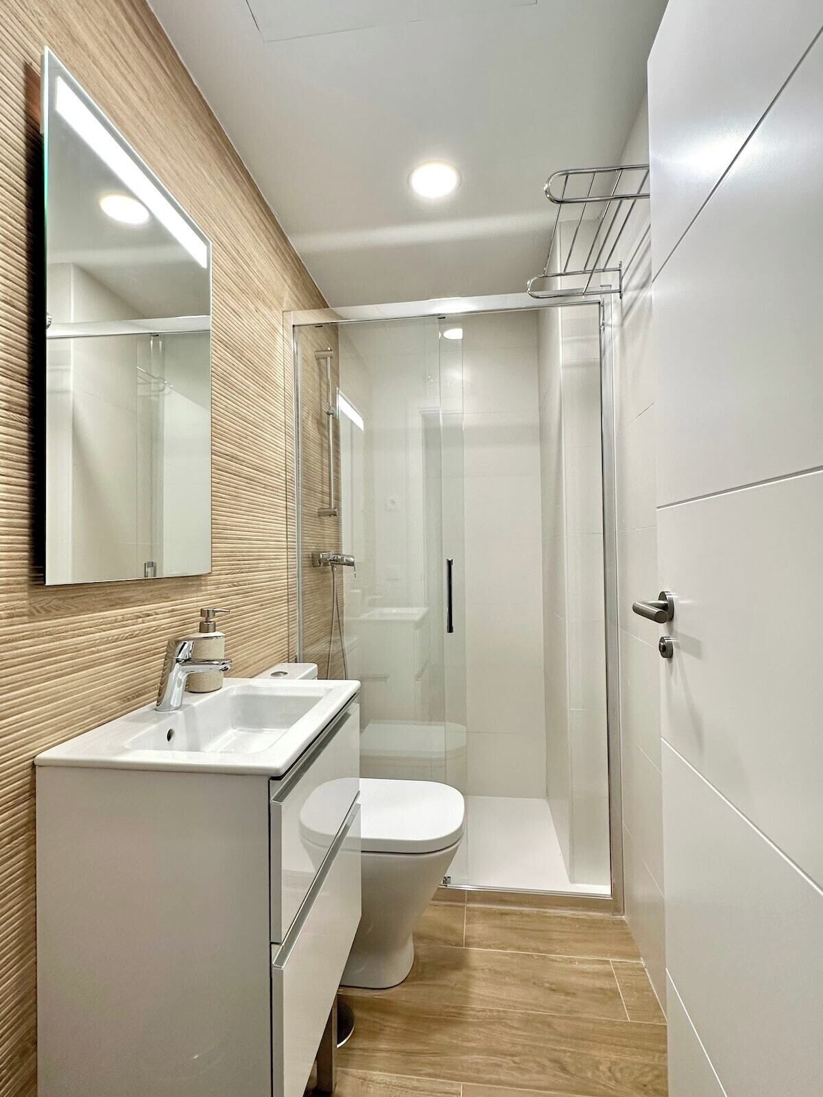 Un baño moderno con ducha envuelta en vidrio, un lavamanos blanco y un inodoro.