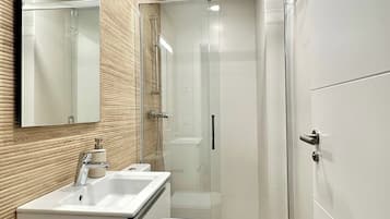 Un baño moderno con ducha envuelta en vidrio, un lavamanos blanco y un inodoro.