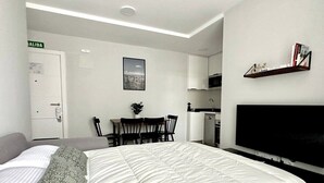 A hotel room with a bed, a TV, a desk with chairs, and a kitchenette.