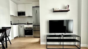 A modern kitchen with white cabinets, a built-in oven, and a dishwasher. There is a black TV stand with a flat-screen TV mounted on the wall above it.