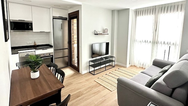 A modern apartment with a dining area, kitchen, living room, and a TV.