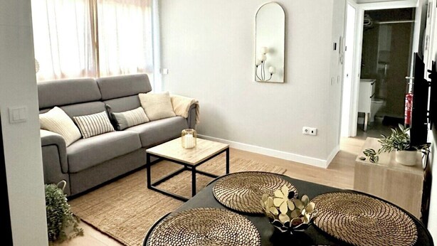 Un salon avec un canapé gris, une table basse et deux petites tables d’appoint en osier.