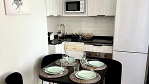 Une cuisine compacte avec des meubles blancs, un four à micro-ondes, une cuisinière et un réfrigérateur. On y trouve une table à manger, mise avec des assiettes et des verres.