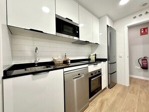 A modern kitchen with white cabinets, a black countertop, stainless steel appliances, and a fire extinguisher on the wall. - Vivodomo | Free parking, new, spacious & bright (Madrid)