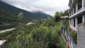 Vista de un valle fluvial con montañas al fondo, un edificio con balcones que dan al río y un puente en primer plano.