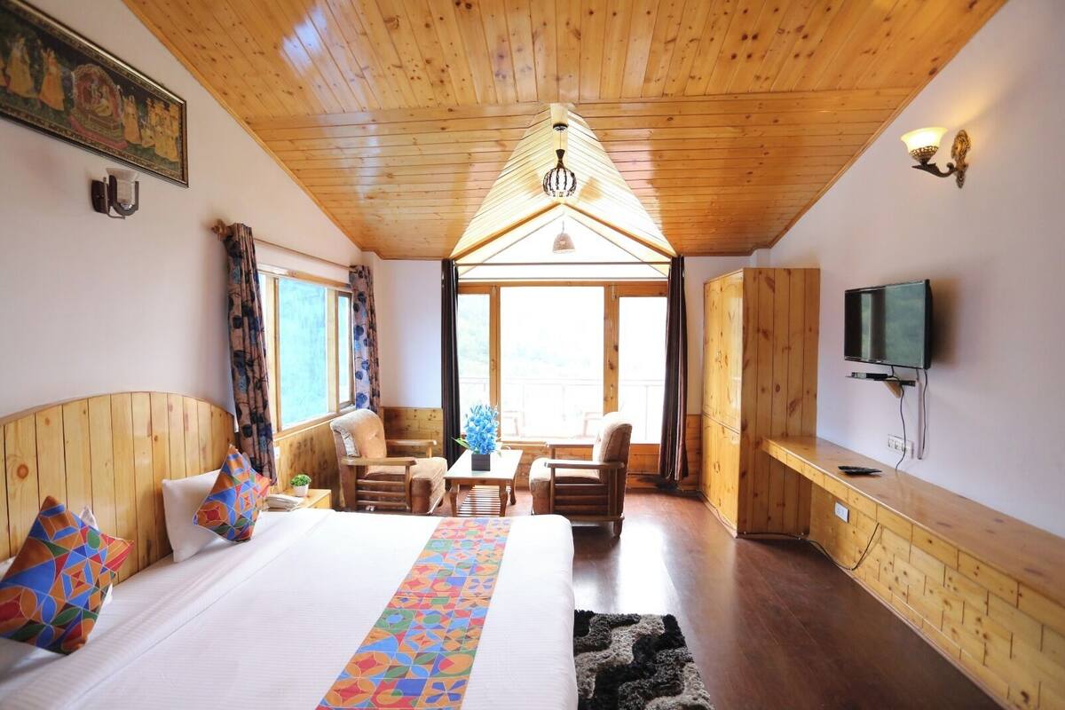 A wooden cabin bedroom with a bed, a desk, a chair, and a TV.