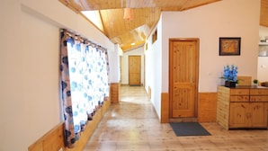 Un pasillo con suelo y paredes de madera, una puerta de madera y una pequeña zona de cocina con fregadero y armarios.