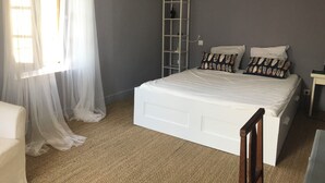 Quarto com cama, guarda-roupa, escada e janela com cortinas leves.