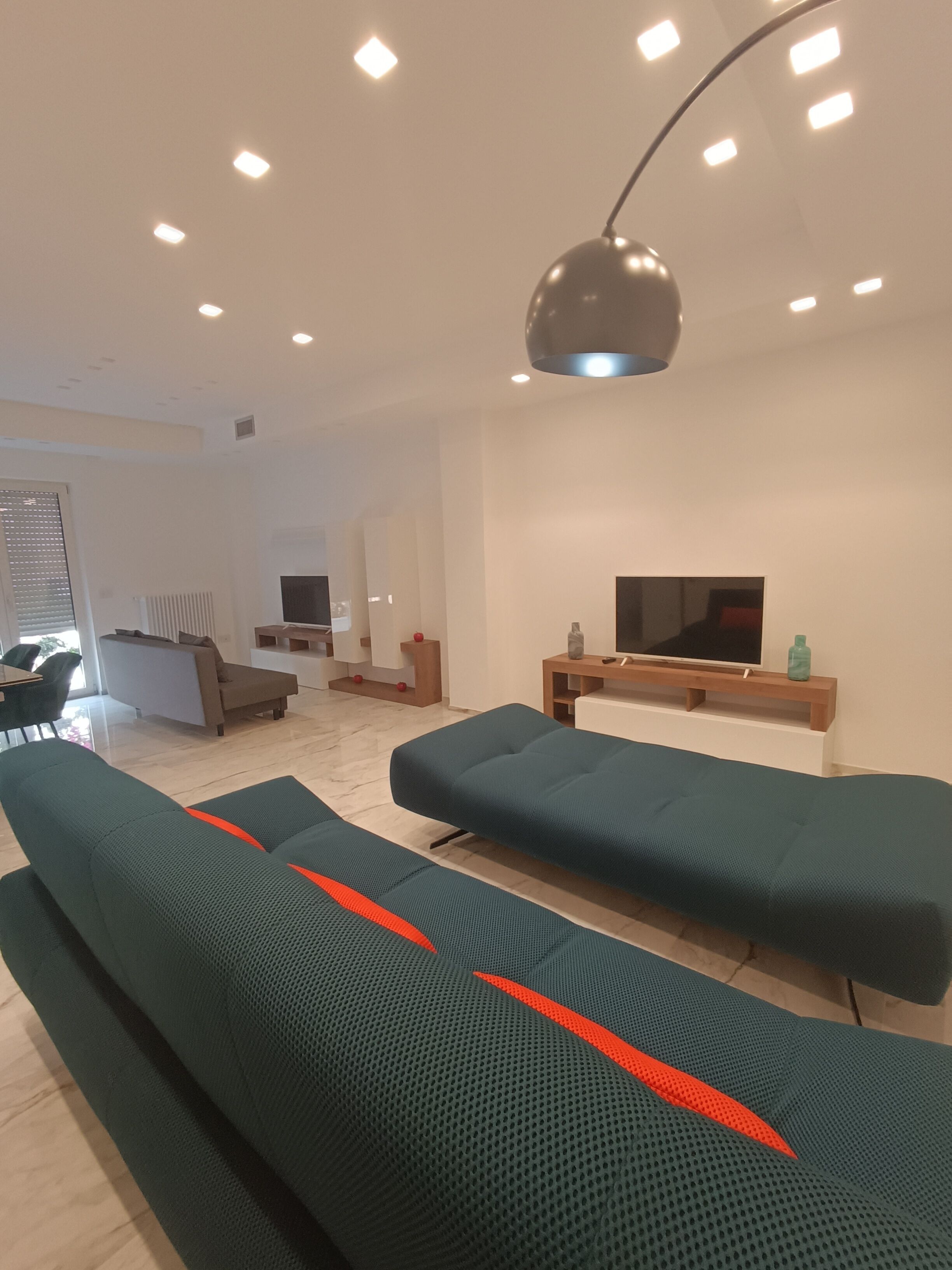 Una sala de estar moderna con un conjunto de sofás, un televisor montado en la pared y una lámpara de techo.