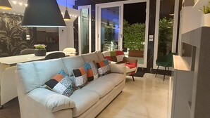 En moderne stue med en hvid sofa, et spisebord, og et køkken der ses igennem glasdøre.