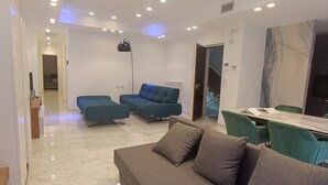 En moderne stue med en grå sofa, turkise lænestole og et spiseområde med et bord og stole.