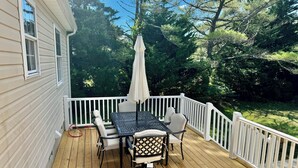 A wooden deck with a table and chairs, surrounded by a white railing, overlooking a wooded area. - Cottage on Snug Harbor, minutes from O.C. beaches, Berlin, and Assateague.  (Berlin)