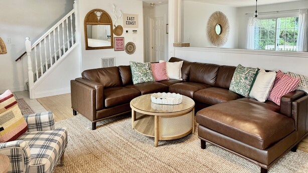 A living room with a brown leather sectional sofa, a round coffee table, and a staircase with white railings. - Cottage on Snug Harbor, minutes from O.C. beaches, Berlin, and Assateague.  (Berlin)