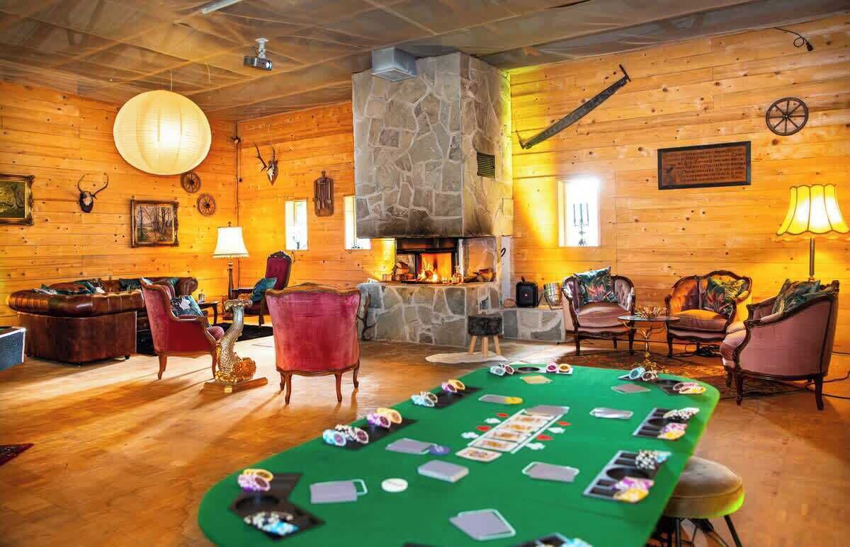 Una habitación acogedora con chimenea, paredes de madera y una mesa de fieltro verde con cartas de juego.