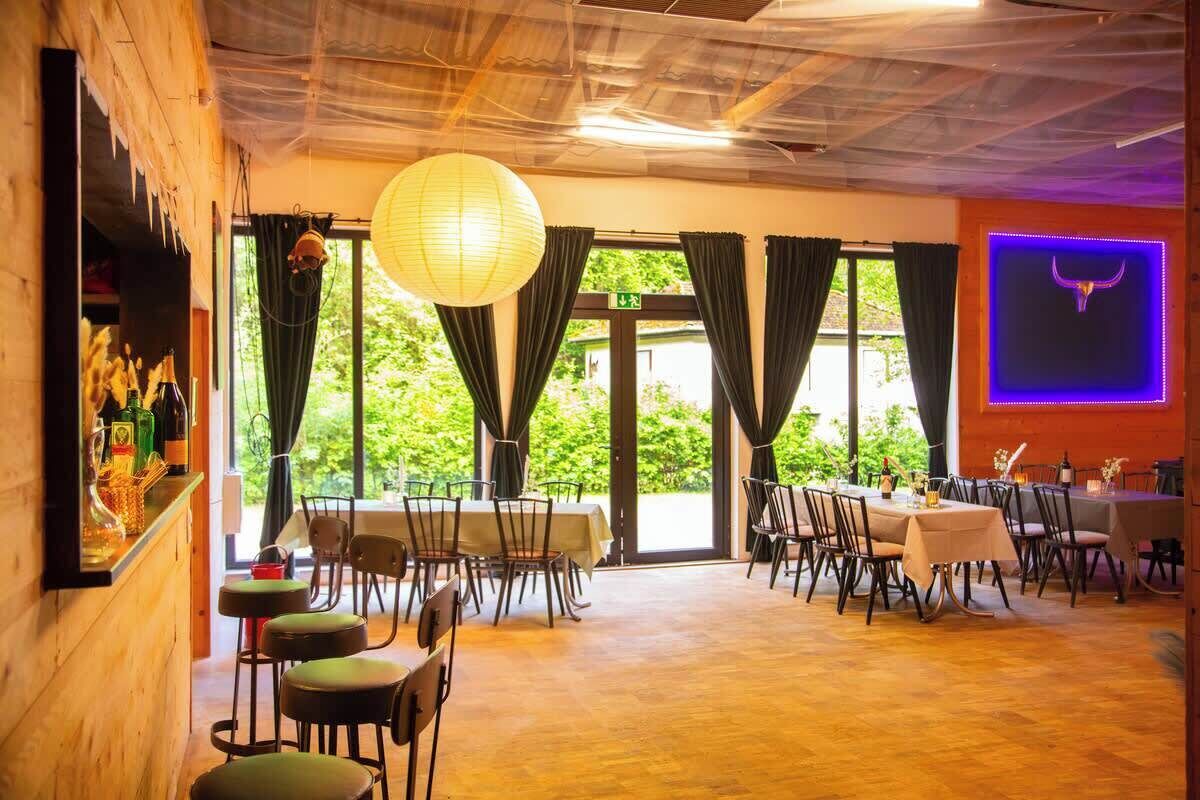 A restaurant with a wooden interior, large windows, and a bar area.
