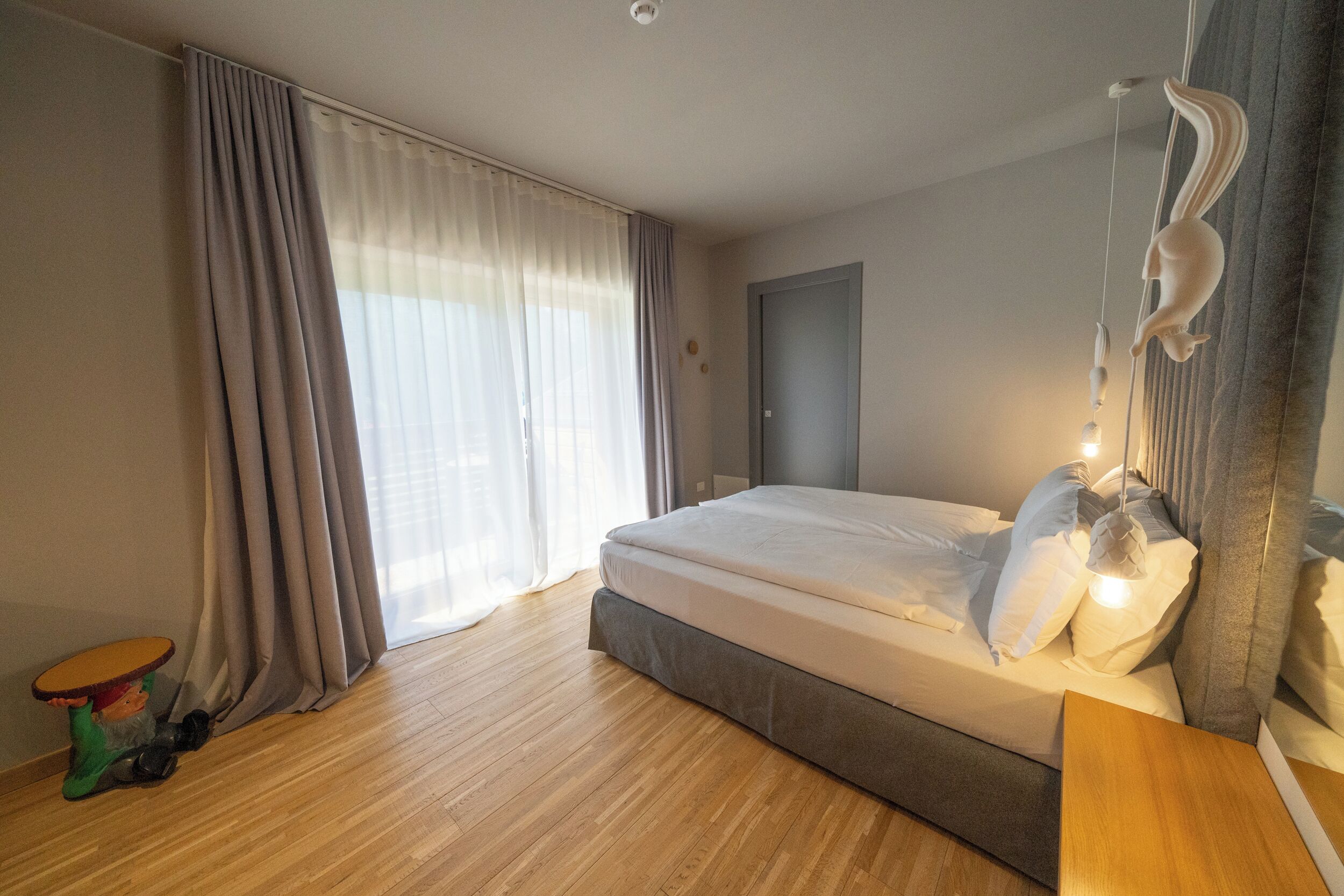 A bedroom with a bed, curtains, a table, and a hanging light fixture.
