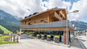 A modern hotel with a wooden facade, large windows, and a mountain backdrop. - Refined and elegant hotel in the center of Sappada (Sappada)