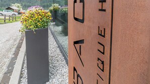A hotel sign with the name "BACH Boutique Hotel" and a view of the surrounding area including mountains and a parking lot. - Refined and elegant hotel in the center of Sappada (Sappada)
