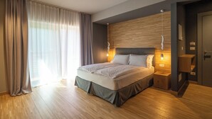 A modern bedroom with a large bed, wooden headboard, bedside tables, and a view of the outdoors through sheer curtains. - Refined and elegant hotel in the center of Sappada (Sappada)