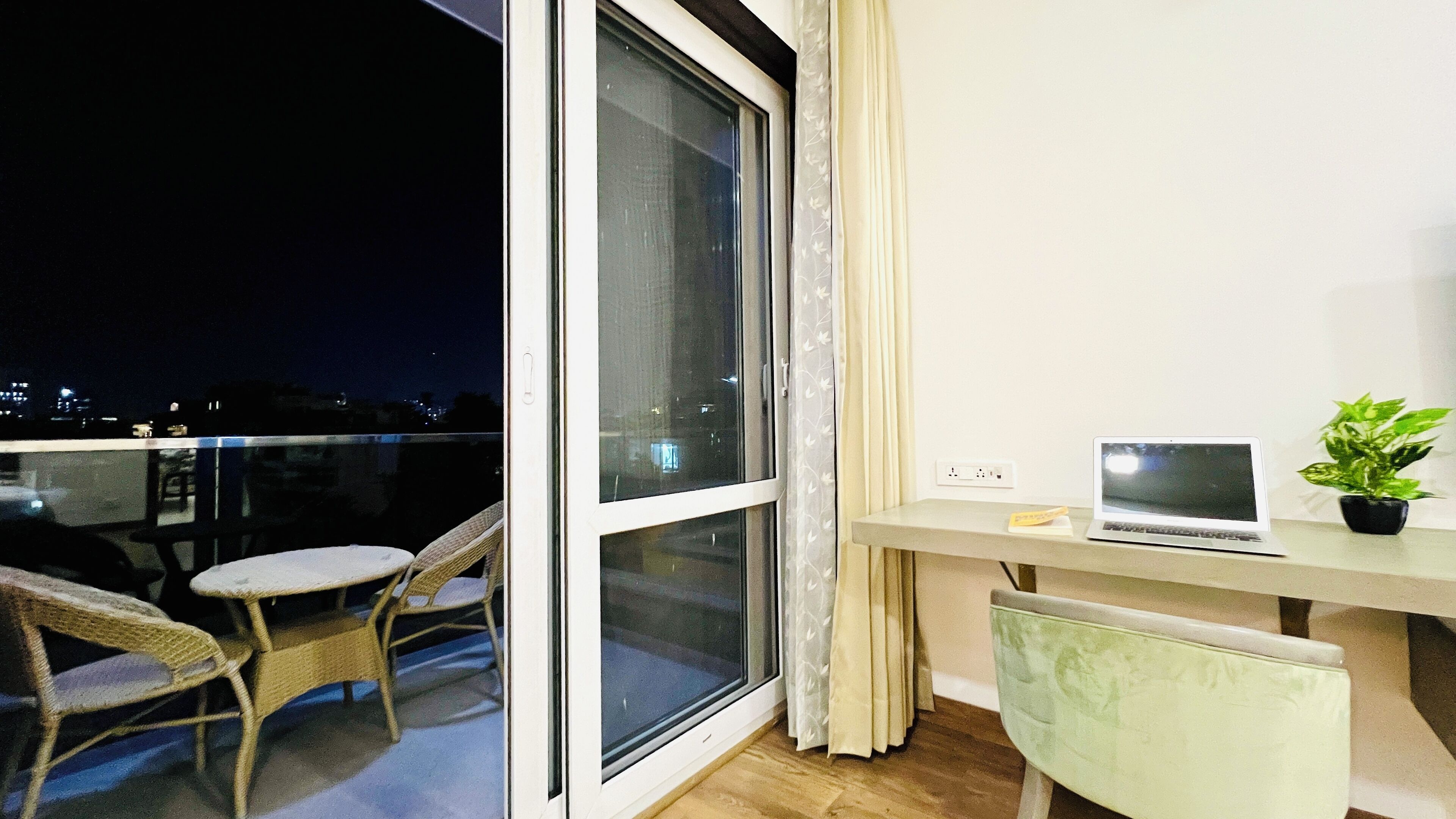 A balcony with a laptop, a potted plant, and wicker chairs.