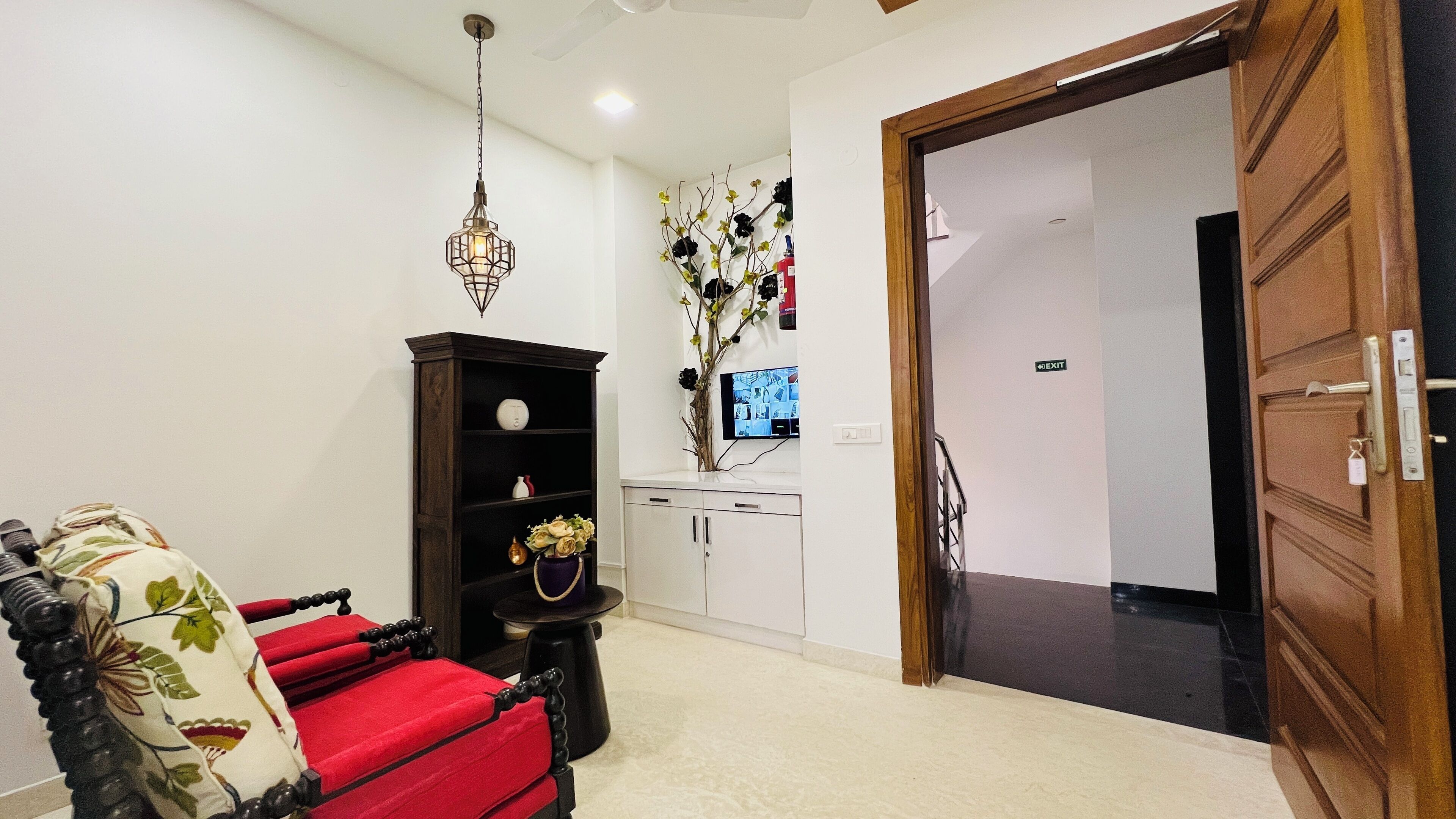 Una sala de estar con un sofá rojo, un aparador de madera, una mesita con un jarrón y una lámpara colgante.
