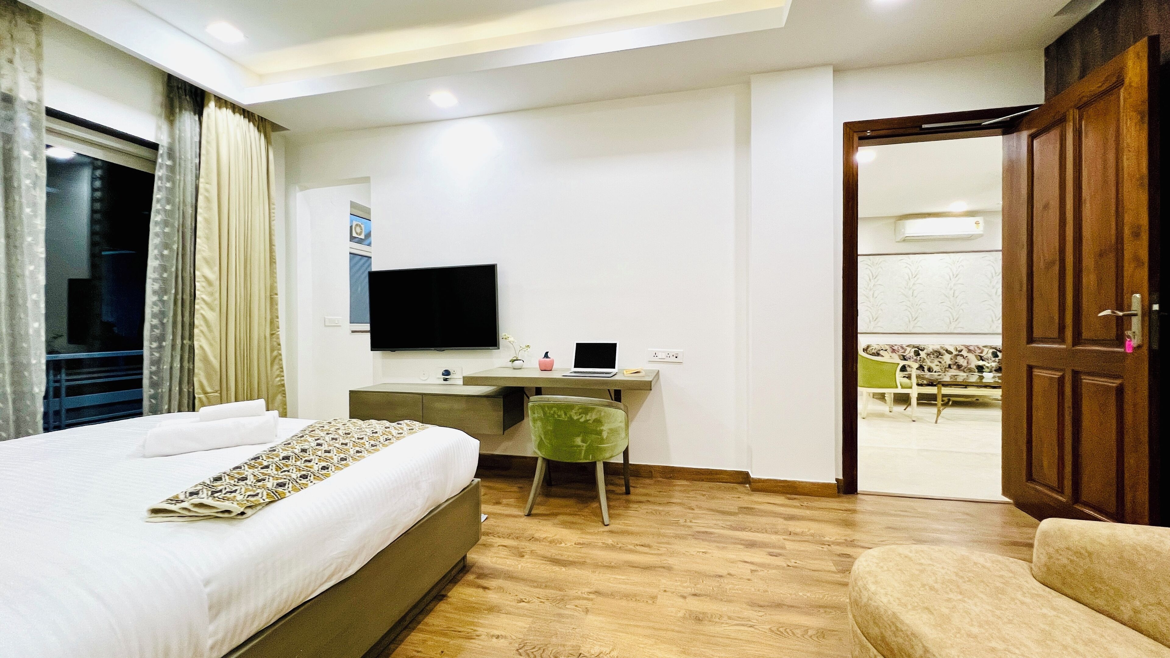 A hotel room with a bed, a desk with a laptop, a chair, a television, and a wardrobe.