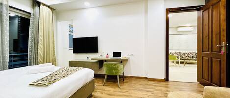 Una habitación de hotel con cama, escritorio con computadora portátil, silla, televisor y armario.