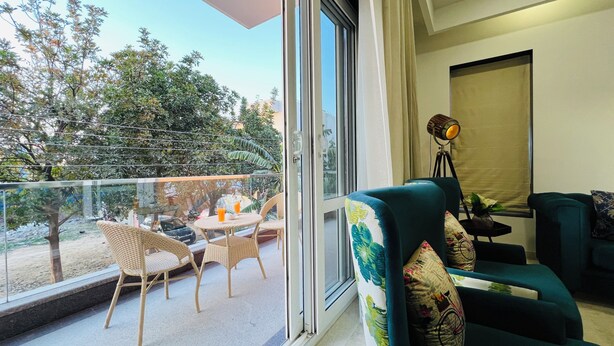 Ein Balkon mit Korbstühlen und einem Tisch, ein Sofa mit gemusterten Kissen sowie eine Stehlampe.