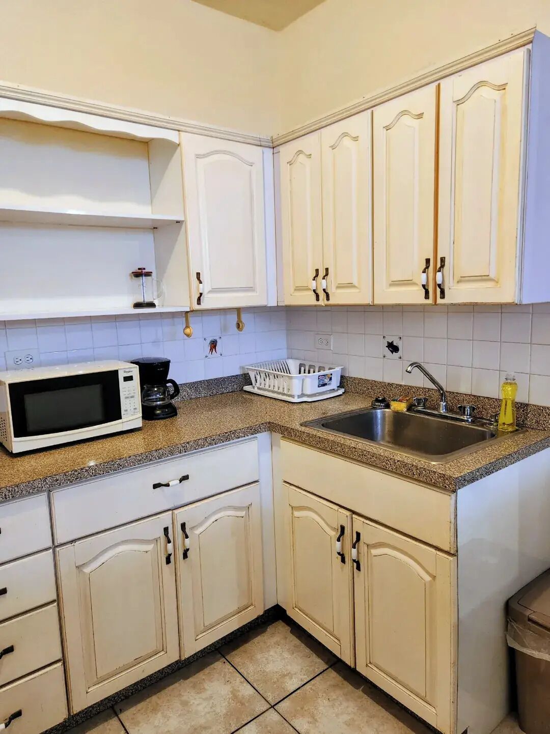 A kitchen with white cabinets, a microwave, a coffee maker, and a sink.