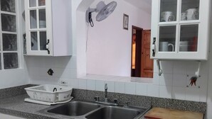 A kitchen with white cabinets, a double sink, a granite countertop, and a wall-mounted fan. - Comfy Haven (Montego Bay)