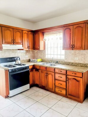 Kitchen features a granite countertop, stainless steel stove, double sink, and window with decorative curtains.