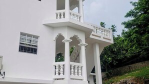 A white building with multiple balconies, a staircase, and a view of greenery. - Comfy Haven (Montego Bay)