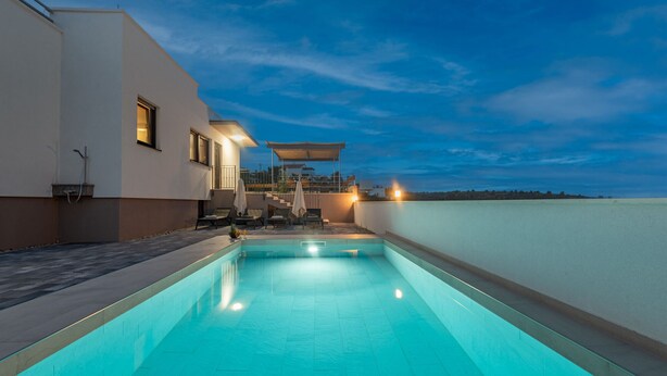 Een buitenzwembad met uitzicht op zee, een overdekt terras en een modern gebouw met een plat dak.