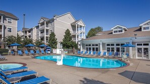 A pool area with lounge chairs and umbrellas, surrounded by multi-story buildings with balconies.