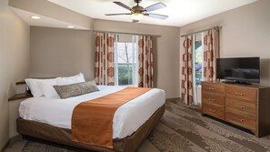A hotel room with a bed, a TV, a ceiling fan, and a view of the outdoors.