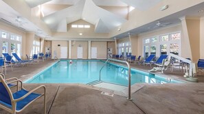 A large indoor swimming pool with blue chairs and a ceiling with geometric patterns.