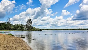 Tyyni järvi, jossa on hiekkaranta, puita ja pilvinen taivas.
