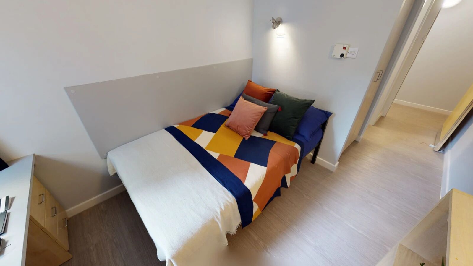 A small, neatly arranged bedroom with a bed, pillows, and a bedside table.