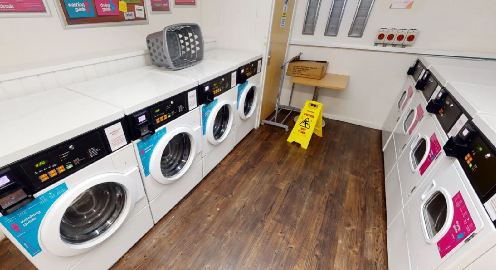 A laundry facility with multiple washing machines, a caution sign, and a control panel.