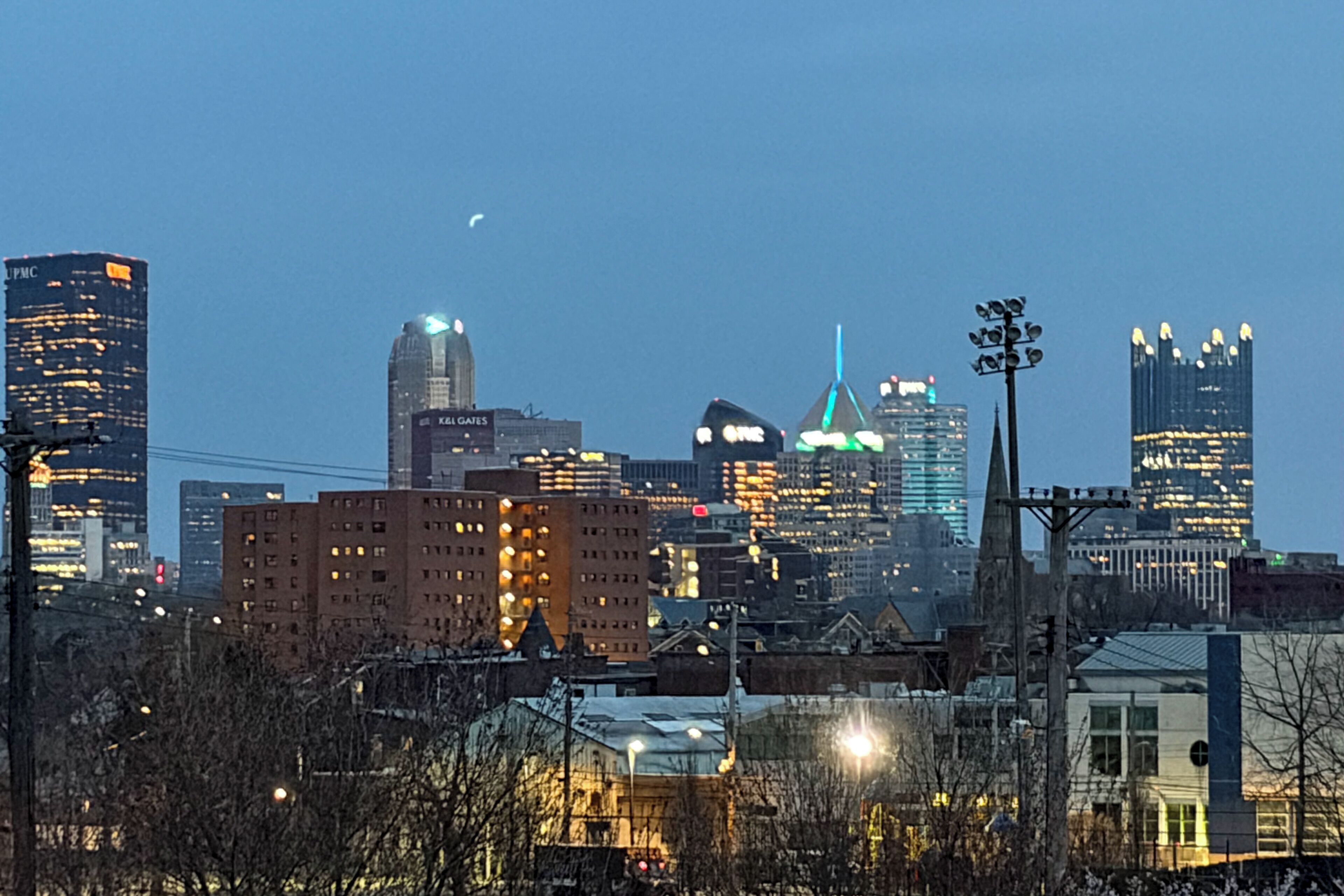 Une vue sur les gratte-ciel d’une ville au crépuscule, avec des bâtiments illuminés et un ciel dégagé.