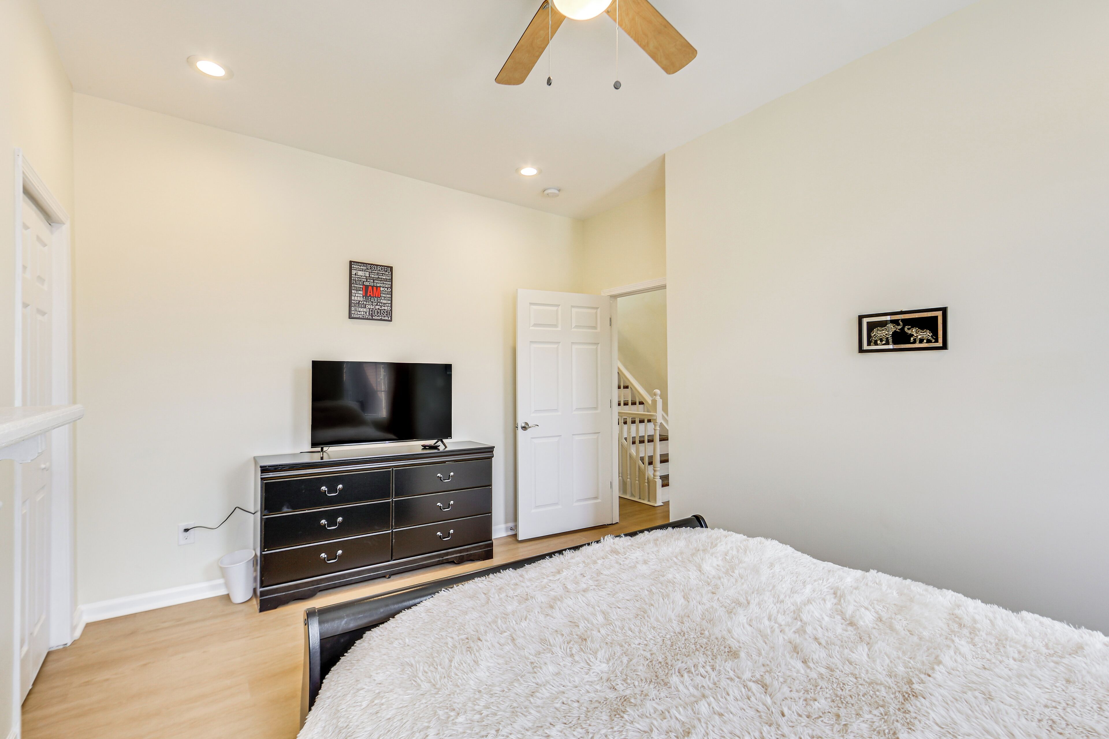 A bedroom with a white fluffy bed, a black dresser, a television, and a white door leading to a staircase.