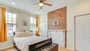 Un dormitorio con cama, una banca, ventilador de techo, pared de ladrillo y chimenea.