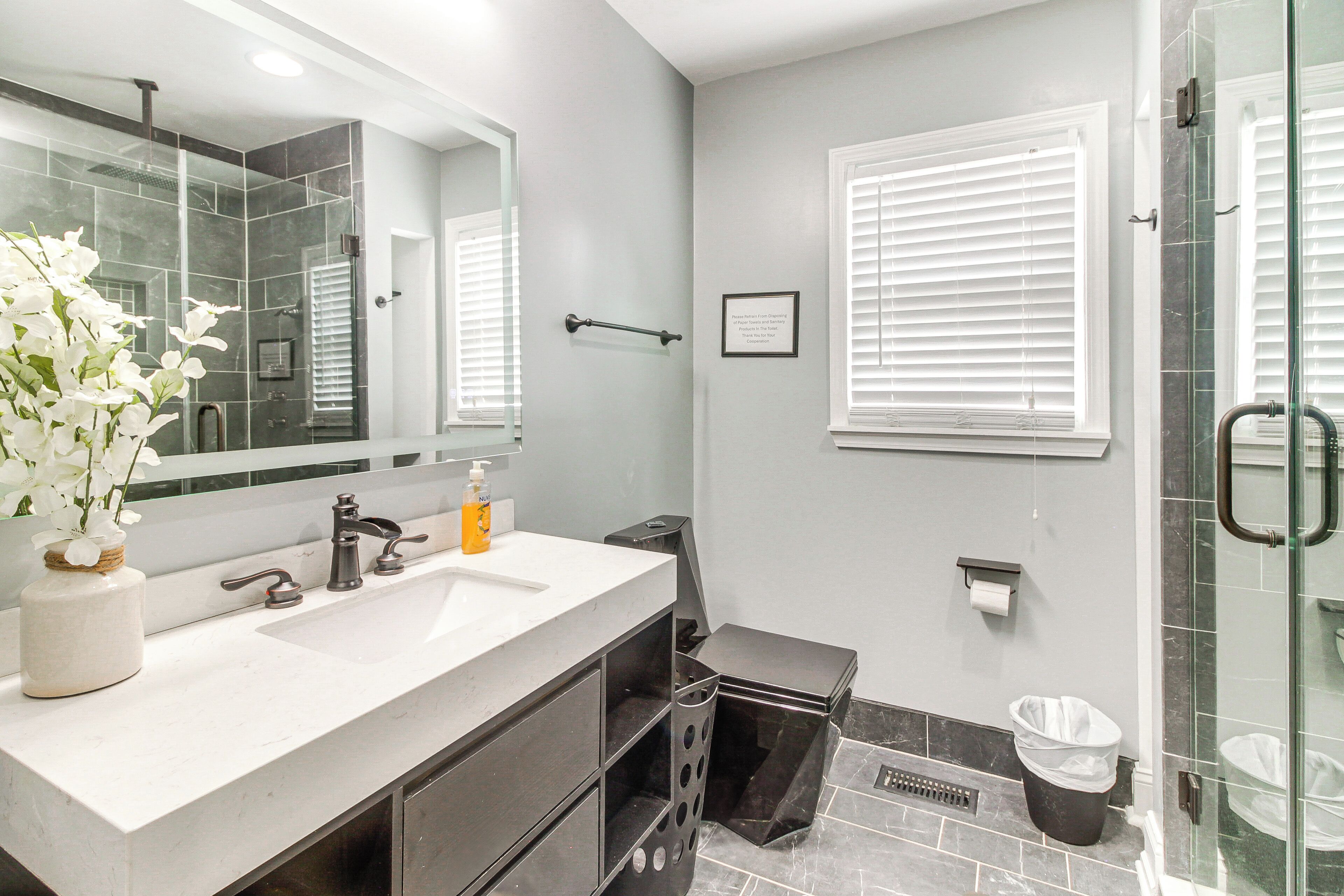 A modern bathroom with a large mirror, two sinks, a shower, and a glass-enclosed shower area.